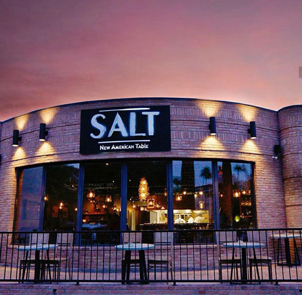 One of the restaurants in McAllen is facing the street, the pink bricks reflecting the light of the pink and yellow hues of the sunset while bright white letters on its black sign read ‘SALT - New American Table.’