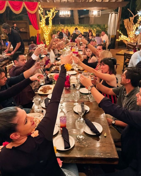 Families cheer by clinking their glasses together as they sit at large dining tables at a restaurant in McAllen immersed in an environment filled with vibrant yellow walls and lit-up decor.