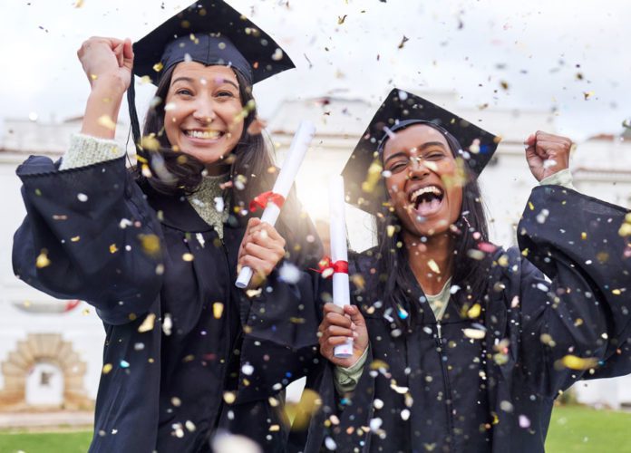 Two young women in McAllen are smiling, dressed in black graduation gowns while confetti falls all over them.