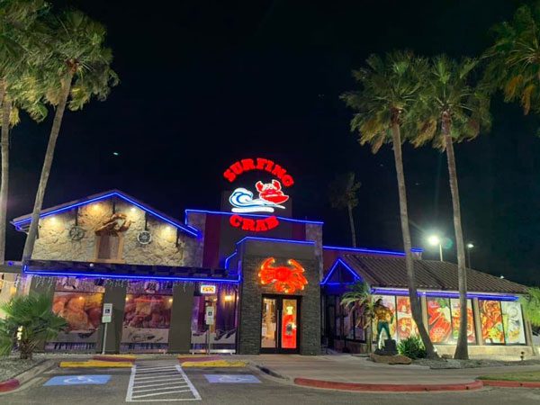 One of the seafood McAllen restaurants at night lit up with blue and red lights facing the empty parking lot with its bright red sign glowing in bold letters, ‘SURFING CRAB.’